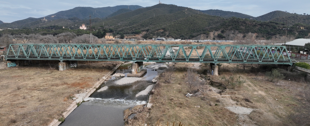 Puente de celosía verde sobre la riera con la sierra al fondo. Fotografía aérea con dron de VISUAIR